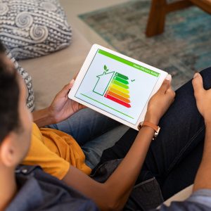 Rear view of indian couple checking on digital tablet housing energy efficiency rate. Young couple searching new green house on digital tablet. Husband embracing wife while checking the energy efficiency status of their home.