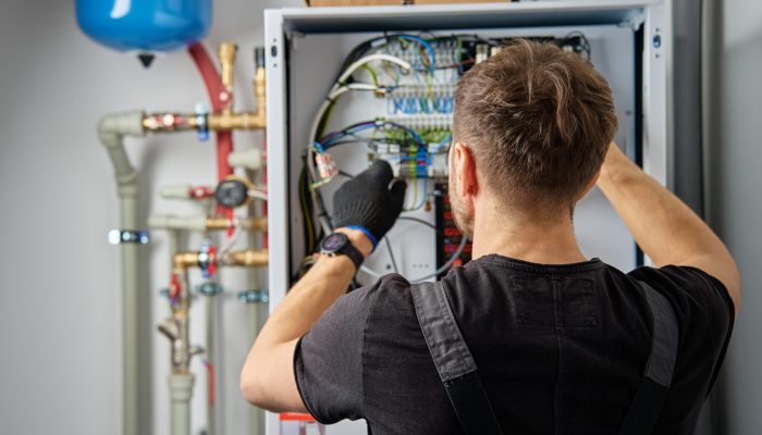 Technician working on internal wiring of heat pump, inspecting electrical connections. Specialist servicing heating and cooling system. Electrician with screwdriver tightening screws on control panel
